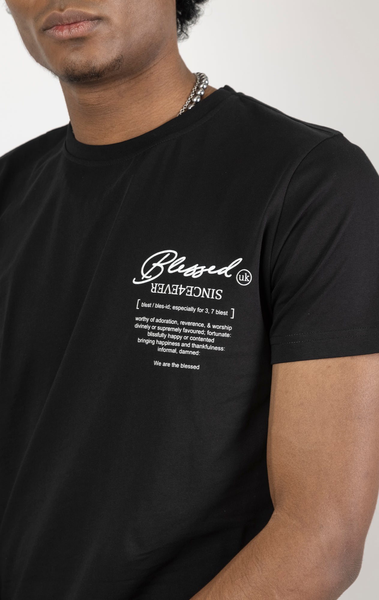 Men's regular fit t-shirt in black. The shirt features a slightly elongated sleeve, a fitted neckline, and a straight body. It has a "Forever a Saint, Never a Snake" digital print on the back with 3D "blessed" embroidery. Made from 100% cotton. A "blessed" slogan is printed on the inner neck binding and a woven side seam tab with "blessed" is also included. The front features a "blessed" with a strikethrough design and the back neck features a signature "blessed" script print.